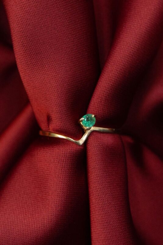 Anillo de oro 18k con esmeralda verde sobre tela roja recogida en pliegues elegantes.
