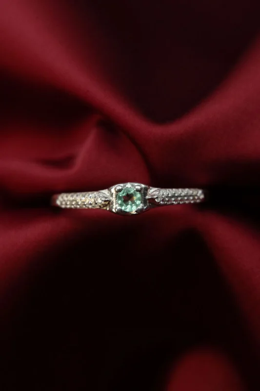 Anillo en plata ley 925 con esmeralda central y circones en el brazo, diseño único, fotografiado sobre tela roja.