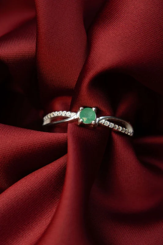 Anillo de plata ley 925 con esmeralda natural y circones, sobre fondo de tela roja.