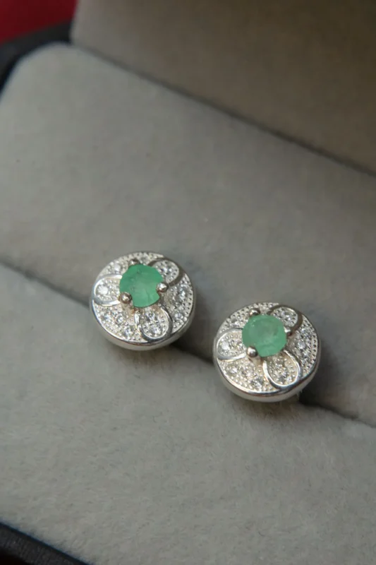 Aretes en plata ley 925 con esmeralda central y circones, sobre estuche gris.
