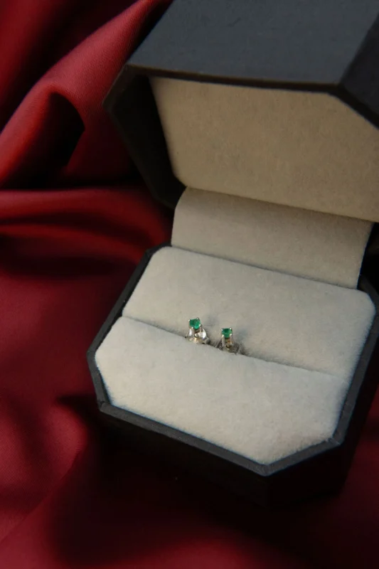 Aretes en plata ley 925 con esmeraldas, presentados en estuche gris sobre fondo de tela roja.