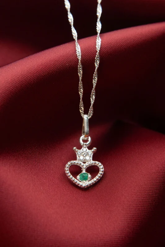 Dije de plata ley 925 en forma de corazón con corona, circones y esmeralda natural sobre fondo de tela roja.