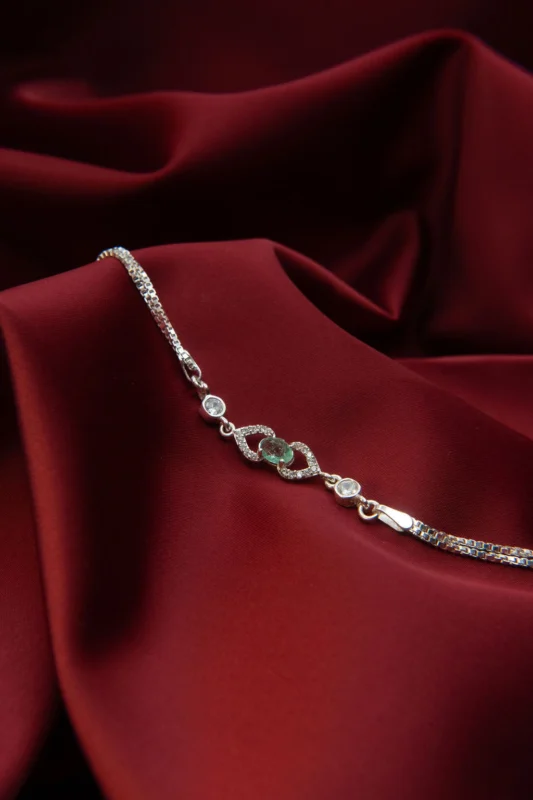 Pulsera en plata ley 925 con esmeralda natural central y circones brillantes, sobre fondo de tela roja.
