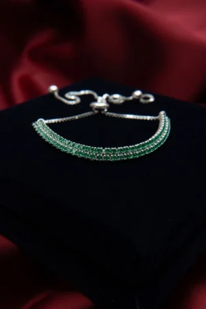 Pulsera tipo tenis doble carril en plata ley 925 con circones verdes, presentada sobre fondo negro y rojo.