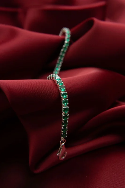 Pulsera tipo tenis doble carril en plata ley 925 con circones verdes, presentada sobre fondo negro y rojo.