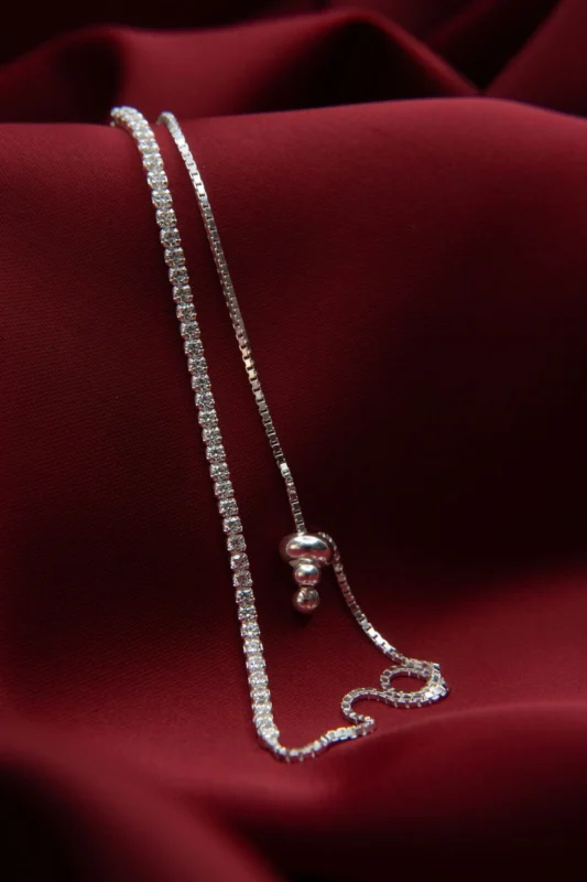 Pulsera tipo tenis carril sencillo en plata ley 925 con circones blancos, presentada sobre fondo de tela roja.