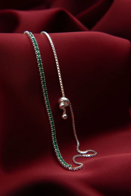 Pulsera tipo tenis carril sencillo en plata ley 925 con circones verdes, sobre fondo de tela roja.