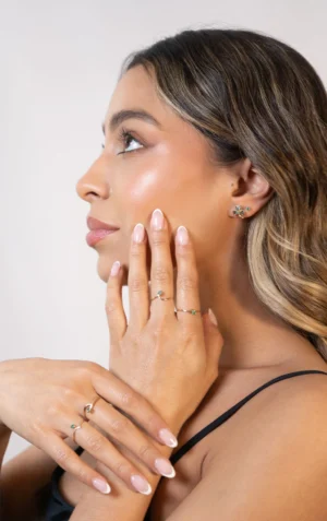 Mujer luciendo aretes y anillos de plata ley 925 con esmeraldas y circones, manos y oreja en primer plano.