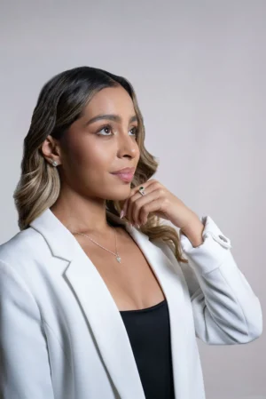 Mujer con blazer blanco y top negro luciendo joyas de plata ley 925 con esmeraldas y circones: aretes, anillo y collar de colibrí.