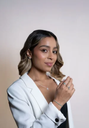 Mujer con blazer blanco luciendo joyas de plata ley 925 con esmeraldas y circones: pulsera, anillos, aretes y collar, fondo neutro.