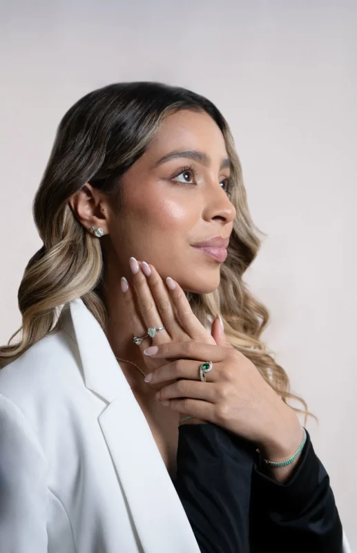 Modelo femenina muestra un elegante primer plano de su oreja y mano, luciendo aretes y anillo elaborados en oro 18 quilates con esmeraldas naturales y circones brillantes. El diseño delicado y sofisticado resalta la belleza y exclusividad de cada pieza. Ideal para quienes buscan un toque de lujo y distinción en su joyería cotidiana.