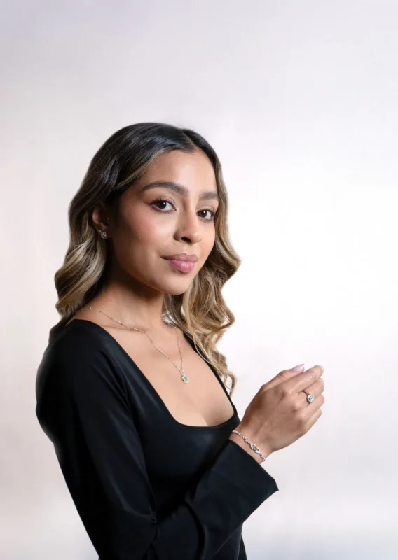 Mujer con cabello suelto luciendo conjunto de joyas en plata ley 925 con esmeraldas y circones, sobre fondo blanco.